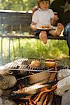 Apples on grill rack over camp- fire, child in background