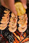 Hand squeezing lemon juice over prawn skewers on grill rack