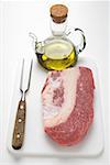 Beef brisket on chopping board, olive oil, meat fork