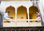 Couple assis sur la rambarde du palais et de l'utilisation de téléphones cellulaires, Neemrana Fort Palace Neemrana, Alwar, Rajasthan, Inde