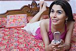 Close-up of a young woman lying on the bed and holding a mobile phone