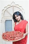 Portrait of a young woman holding a tray of red chili peppers