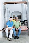 Portrait de deux hommes assis avec un garçon sur une balançoire de porche et souriant