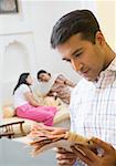 Close-up of a mid adult man reading a newspaper with two mid adult women sitting behind him