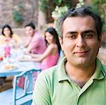 Portrait d'un homme adult mid souriant avec ses amis assis à une table à manger en arrière-plan