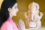 Side profile of a mid adult woman praying in front of a statue of God Ganesha