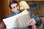 Close-up of a businessman sitting in an armchair and reading a newspaper