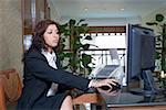 Side profile of a female receptionist working on a desktop PC in a hotel reception