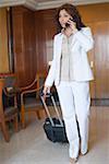 Businesswoman pulling a suitcase and talking on a mobile phone