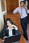 Businesswoman working on a laptop with a businessman talking on a mobile phone in the background