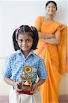 Portrait of a schoolgirl holding a trophy with a teacher in the background