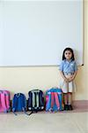 Portrait of a schoolgirl standing near schoolbags in a classroom