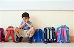 Portrait of a schoolboy crouching near schoolbags and looking sad