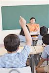 Rear view of a schoolboy in a classroom with his hand raised