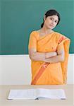 Portrait of a female teacher standing in front of a blackboard with her arms crossed