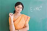 Portrait of a female teacher holding a chalk and standing in front of a blackboard