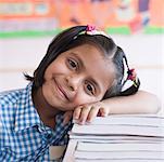 Portrait d'une écolière se penchant sur une pile de bouquins et ricaner