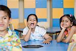 Portrait of a schoolgirl sitting with her friends in a class room and shouting