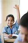 Portrait of a schoolgirl sitting in a classroom with her hand raised