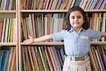 Portrait of a schoolgirl standing in a library with her arms outstretched