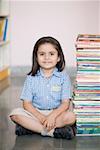 Portrait of a schoolgirl sitting on the floor with a stack of books