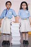 Portrait of two schoolgirls standing with a stack of books