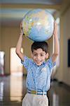 Portrait of a schoolboy holding a globe above his head