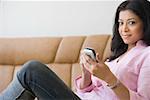 Portrait d'une jeune femme assise sur un canapé et d'un téléphone mobile