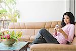 Profil de côté d'une jeune femme assise sur un canapé et d'un téléphone mobile