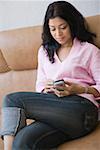 Young woman sitting on a couch and operating a mobile phone