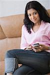 Portrait d'une jeune femme assise sur un canapé et de tenir un téléphone mobile