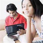 Close-up of a young woman thinking with a young man using a laptop beside her