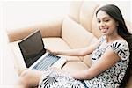 Portrait d'une jeune femme assise sur un canapé et à l'aide d'un ordinateur portable