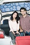Portrait of a young couple sitting in a car trunk and smiling