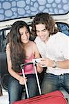 Young couple sitting in a car trunk and looking at a digital camera