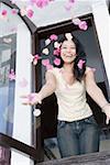 Young woman throwing flowers in air through a window