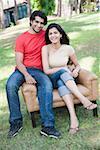 Portrait of a young couple sitting in an armchair in a park and smiling