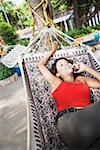 High angle view of a young woman lying in a hammock and talking on a mobile phone