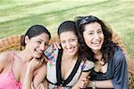 Drei junge Frauen sitzen auf einer Couch in einem Park und lachen