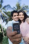 Vue d'angle faible d'un jeune couple en prenant une photo d'eux-mêmes avec un téléphone portable et souriant