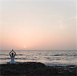 Rear view of a woman practicing yoga on the coast