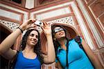 Low angle view of a young woman taking a picture with her friend standing beside her, Taj Mahal, Agra, Uttar Pradesh, India
