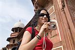 Vue d'angle faible d'une jeune femme tenant un appareil photo numérique et souriant, Taj Mahal, Agra, Uttar Pradesh, Inde