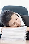 Close-up of a businesswoman leaning on a stack of papers and sleeping