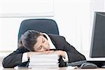 Close-up of a businesswoman leaning on a stack of papers and sleeping