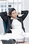 Businesswoman sitting in an office with her hands behind her head