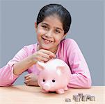 Portrait of a girl putting a coin into a piggy bank and smiling