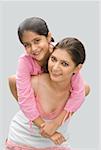 Portrait of a girl riding piggyback on her mother's back and smiling