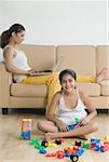 Portrait of a girl playing with building blocks and her mother using a laptop behind her