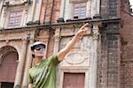 Young man standing in front of a building and pointing, Goa, India